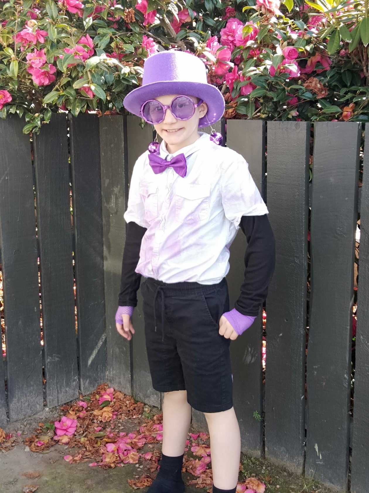 Young boy dressed up in Purple top hat, sparkly bow tie, large round purple glasses and purple gloves.