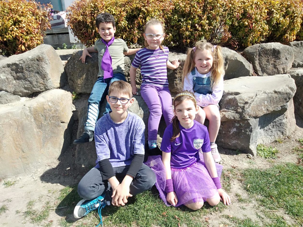 6 young students aged around 5-7 from a primary school gather together for a photo all dressed up in purple costumes