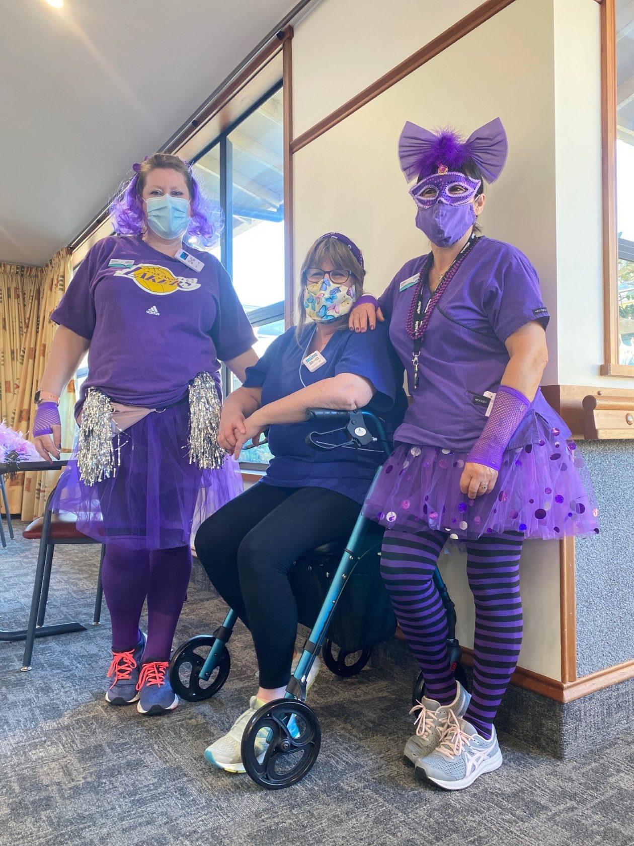 3 staff members from the Croft rest home dressed up in purple costumes pose for a photo