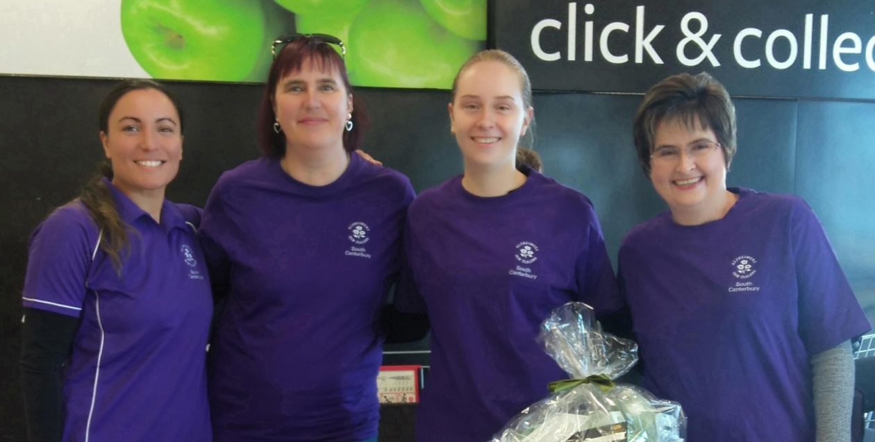 Four women side by side smiling and wearing Alzheimers South Canterbury volunteer t-shirts at a fundraising event.