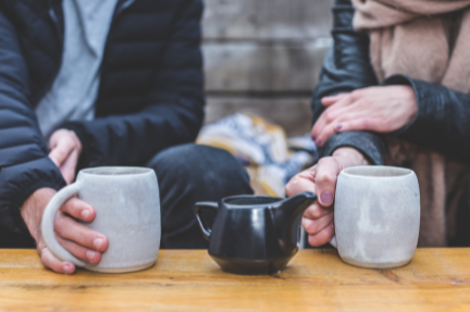 two people sit together with a drinking mug each in their hands