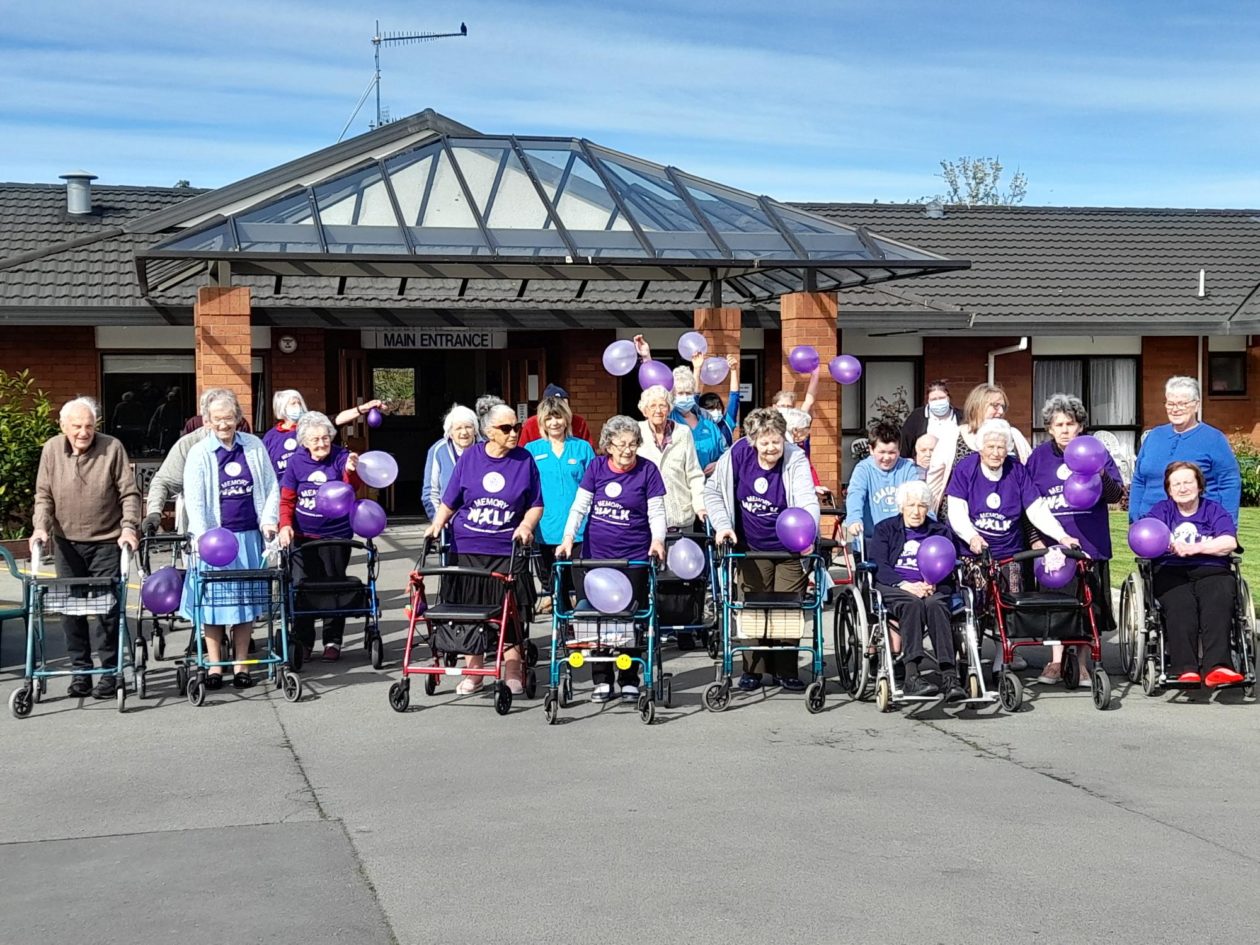 A large group of senior citizens dressed in purple with purple balloons about to go for a walk together