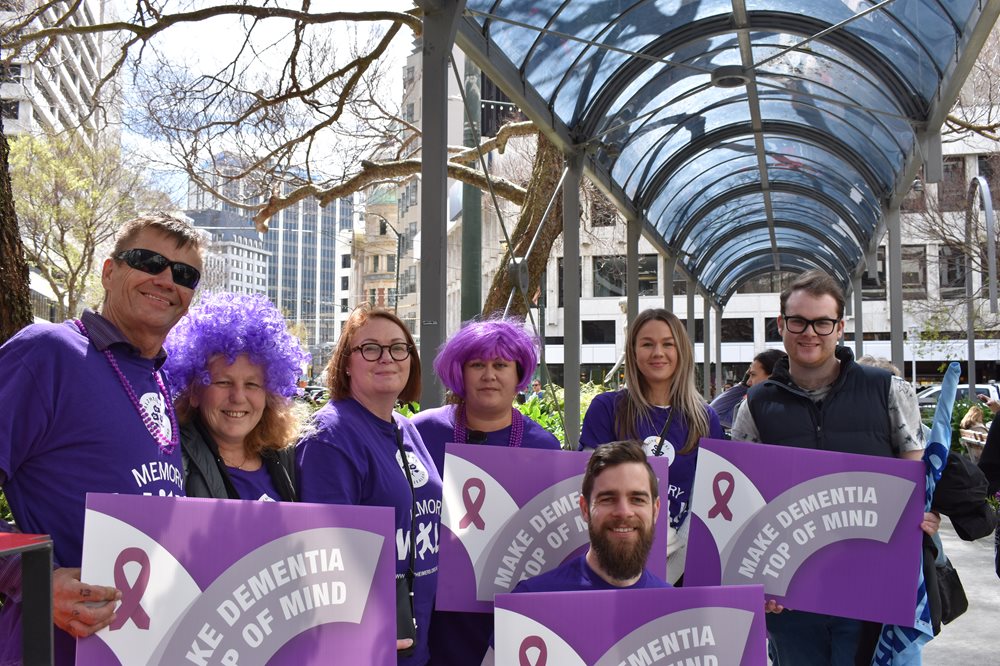 Group of people wearing purple holding signs that read 'make dementia top of the mind'.
