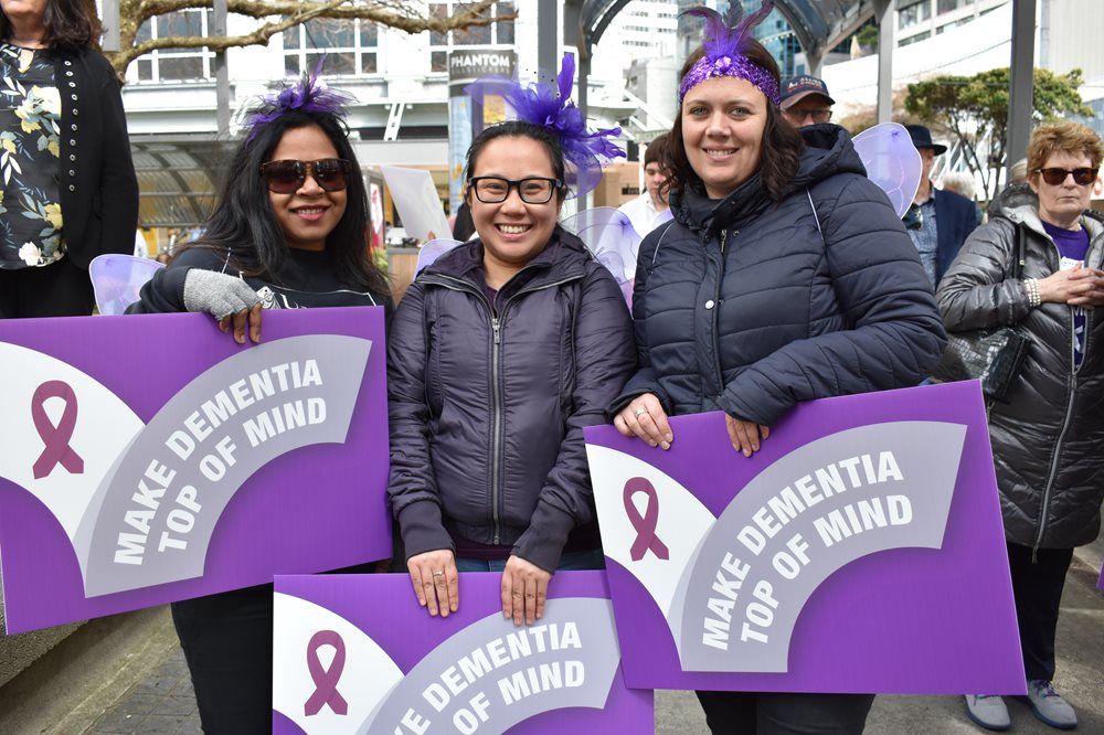 Group of people wearing purple holding signs that read 'make dementia top of the mind'.