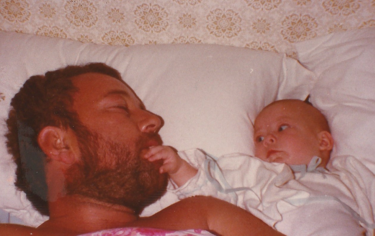 Liam and his dad as a baby lying next to each other in bed