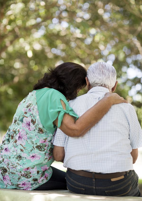 Elderly man sitting with a woman who has her arm around him and her head on his shoulder