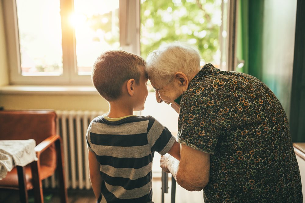 Senior woman bending over and hugging her grandsons arm