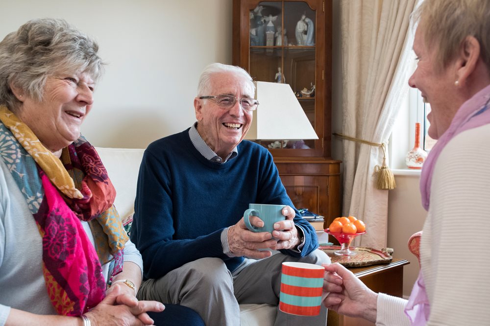 Group of two senior woman and one male drinking tea and laughing.