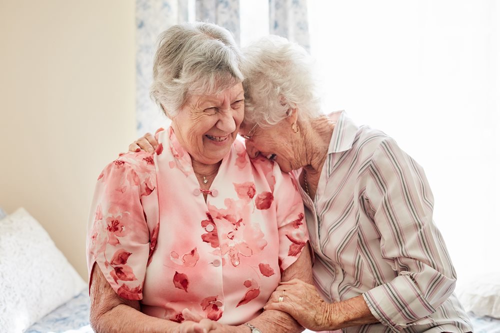 2 senior women laughing together. One is laughing into the other's shoulder.