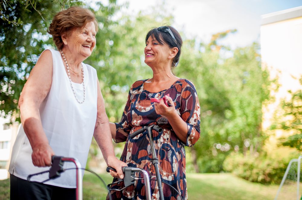 Senior women laughing with another woman while using her walker.