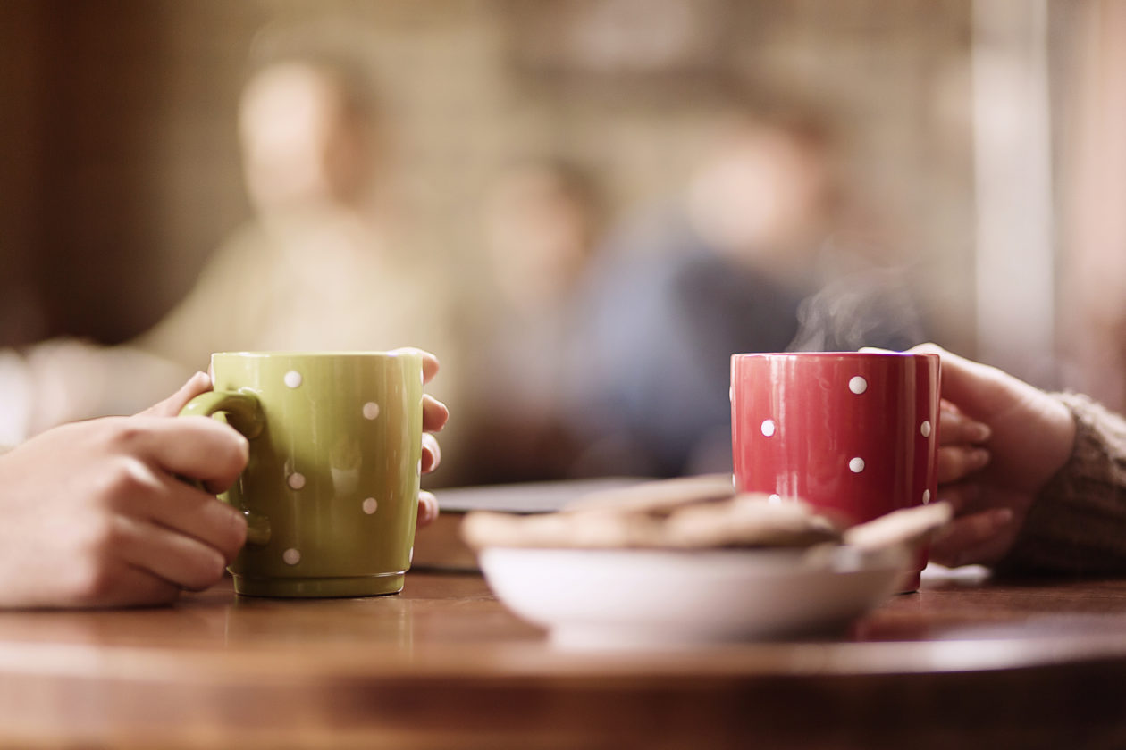 Two people drinking hot cups of tea. The in a bowl of cookies in the foreground 