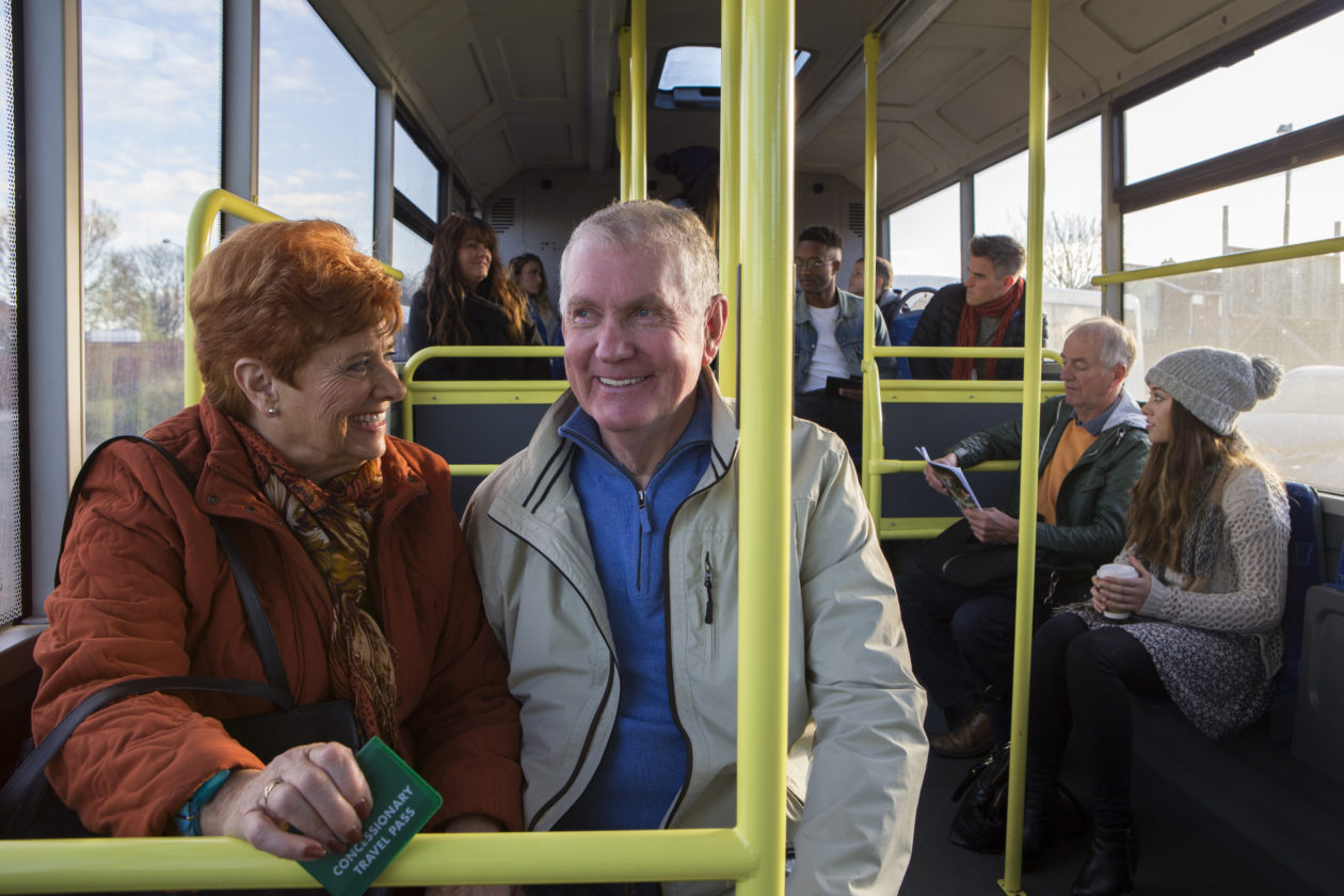 Elderly couple sitting on bus together smiling 
